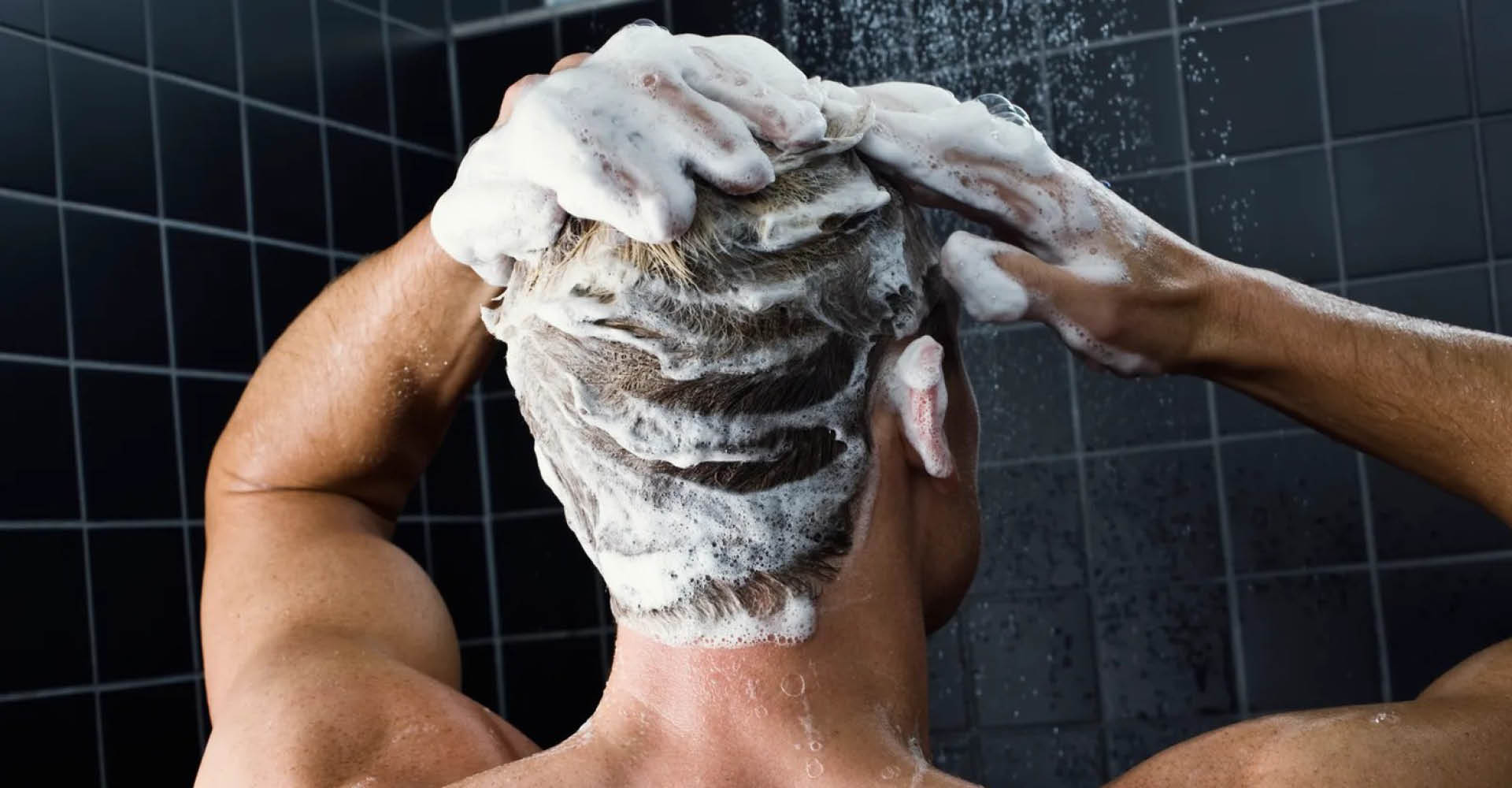 Immagine di un uomo sotto la doccia, visto di spalle, con i capelli molto insaponati